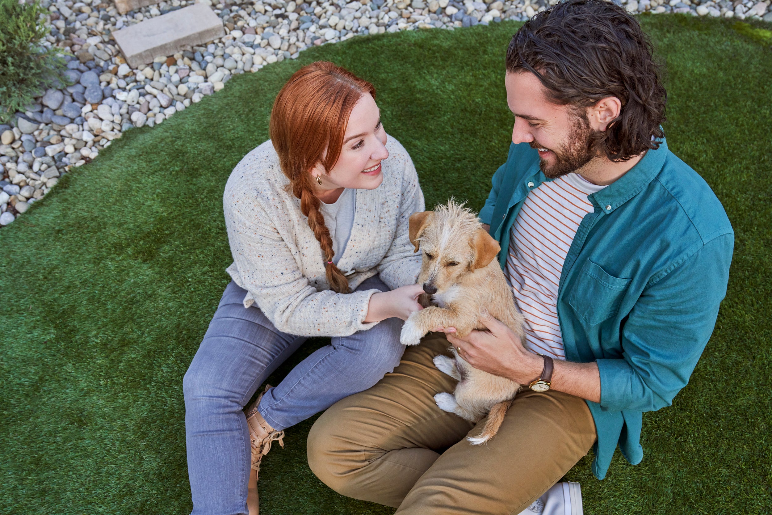 Two people sitting on grass petting yellow dog
