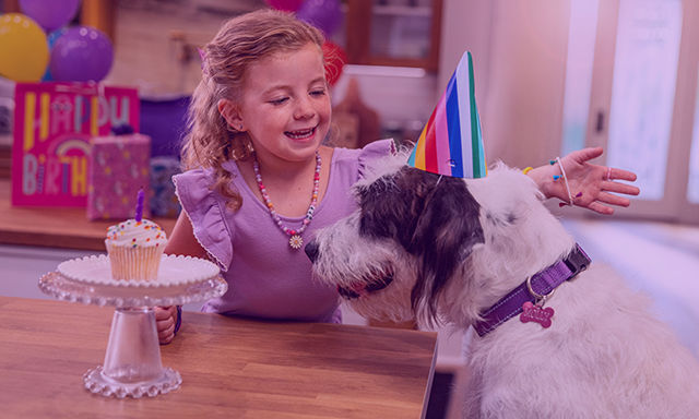 Little girl smiling at her dog at her birthday party.